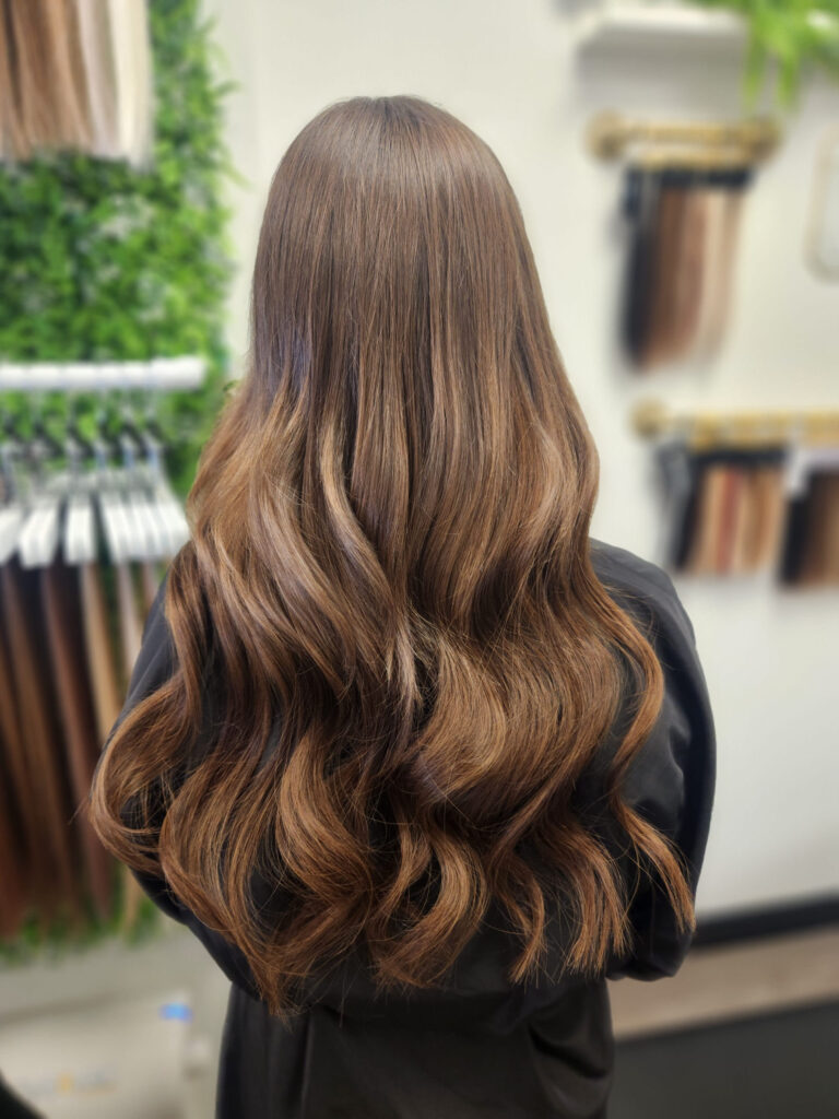 Back view of long, wavy brunette hair with caramel highlights in a salon